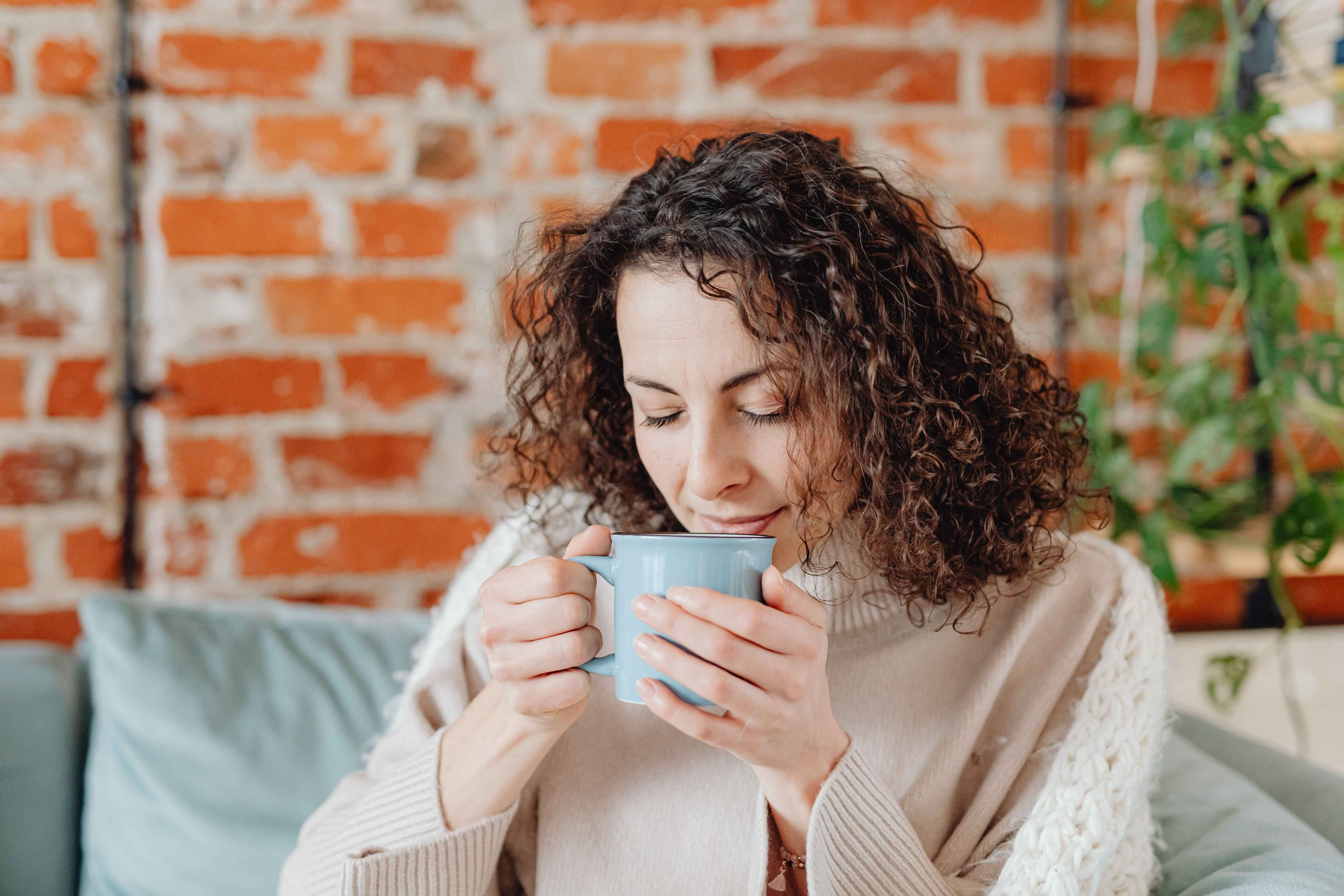A woman holds a mug of tea close to her face as she savors the aroma.