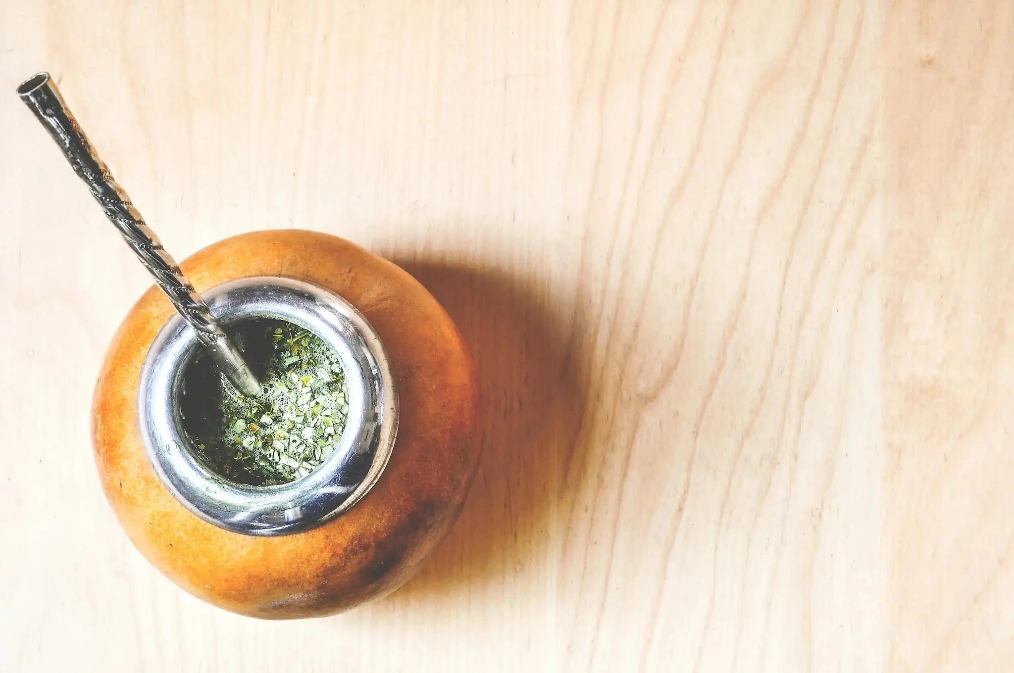 yerba mate in a natural gourd with a metal rim and metal bombilla on a light wood background