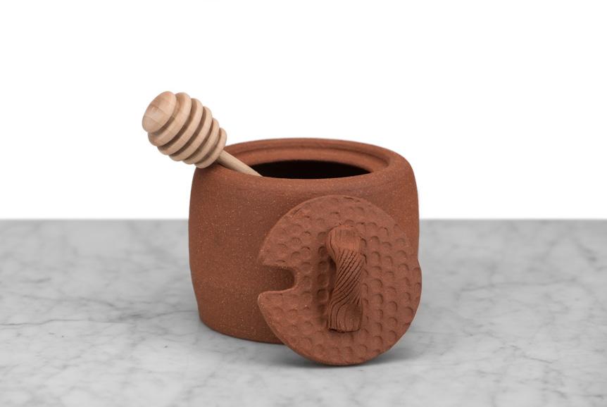 clay honey pot with dipper and top resting on its side