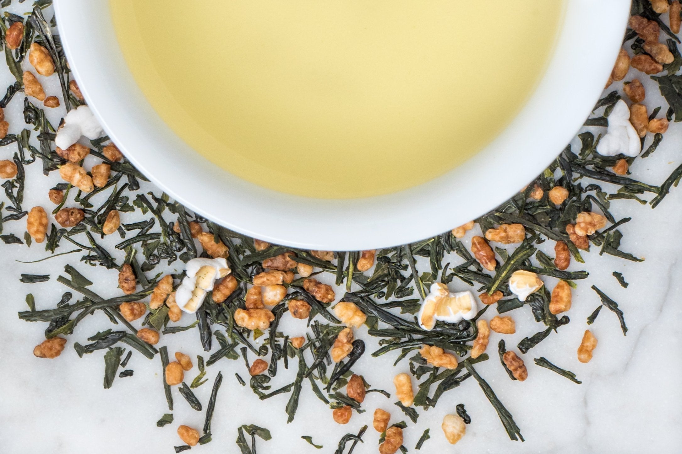 loose leaf genmai cha green tea surrounding a white cup of brewed green tea
