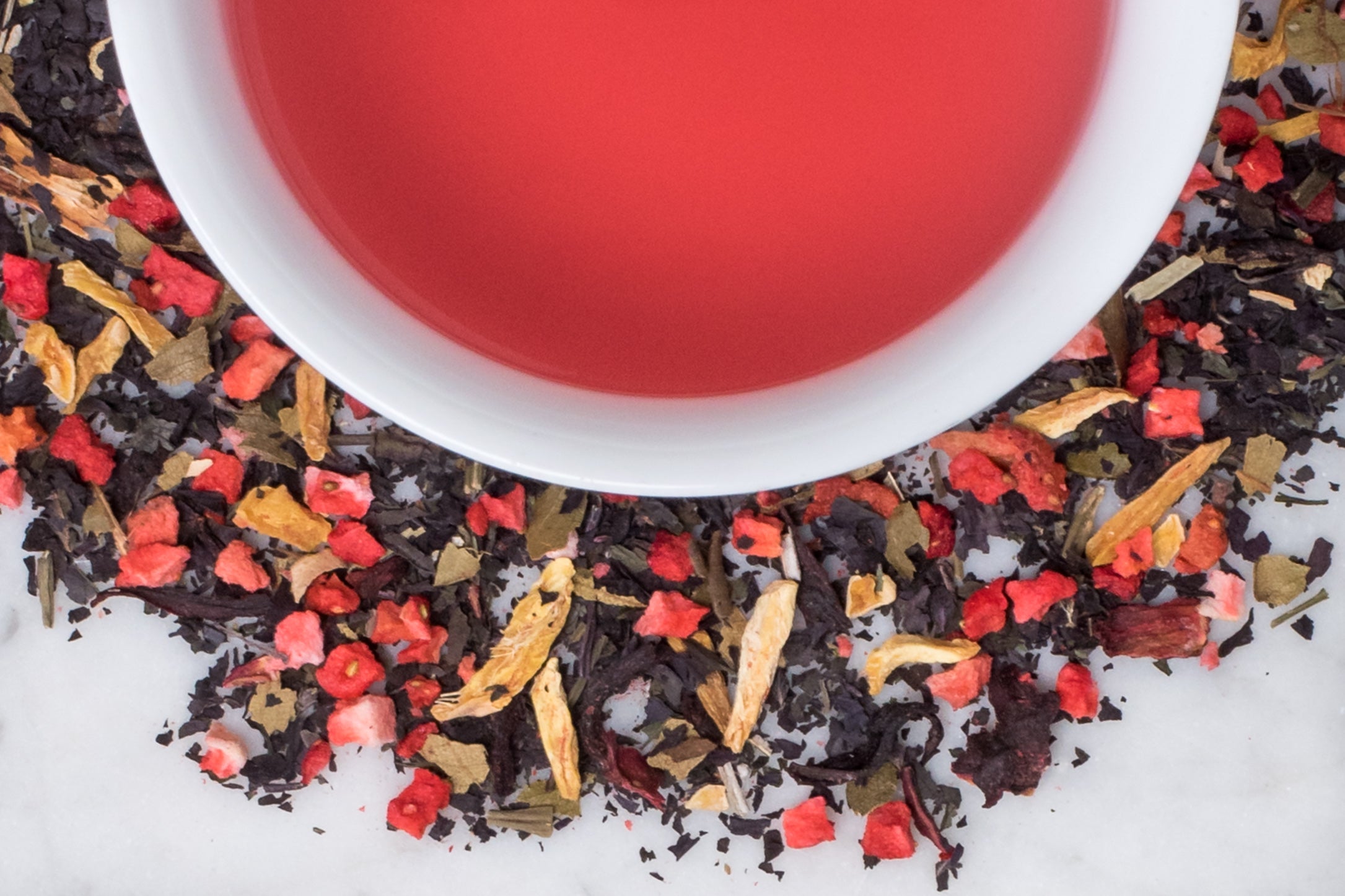Shiso Pretty leaves and brewed tea. Dried strawberry pieces, shiso (japanese mint), ginger, and hibiscus leaves surround a cup of vibrantly pink brewed tea.
