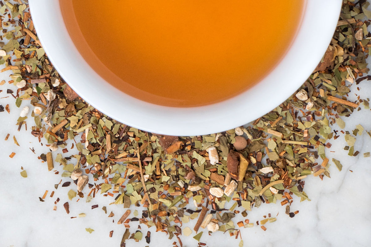 loose leaf energizing herbal tisane for focus surrounding a white cup with brewed tea
